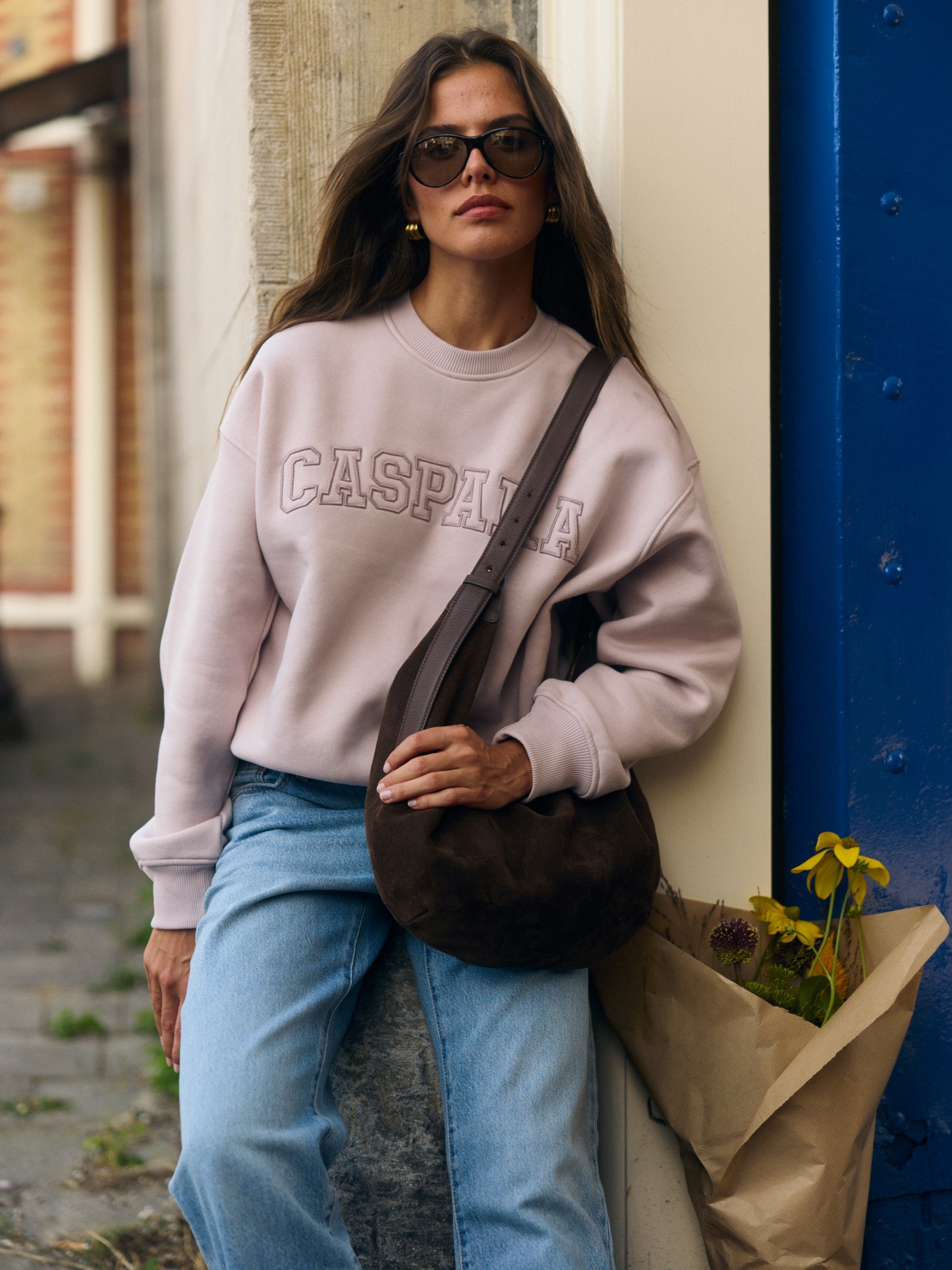Woman wearing a dusty pink CASPARA outline crewneck sweatshirt and blue jeans outdoors.